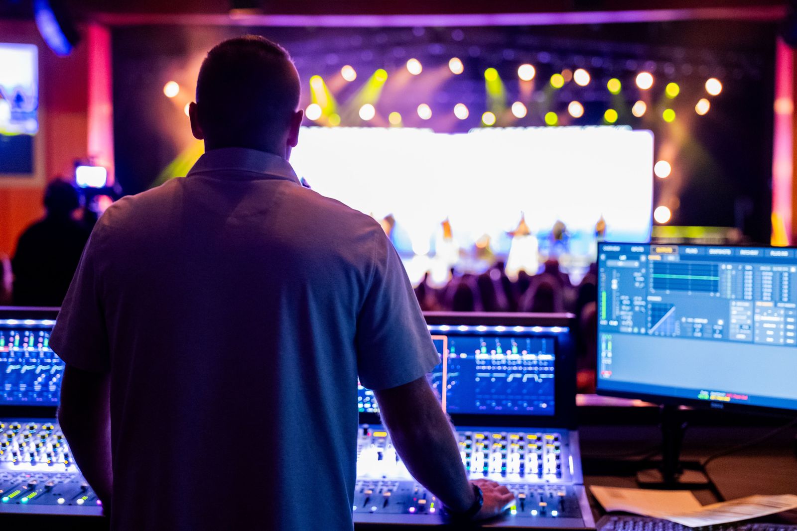 Sound engineer working at a mixing desk in front of a lit stage